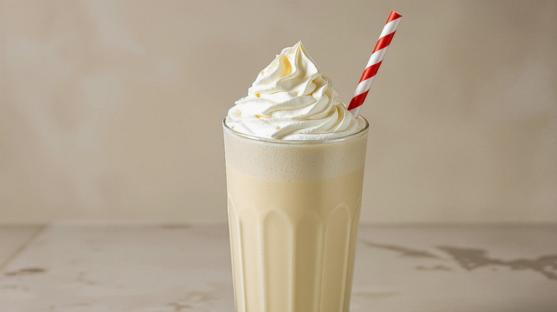 Vanilla milkshake in tall glass with whipped cream and striped straw