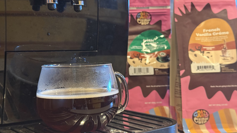 Cup of coffee under machine with bags of coffee in background