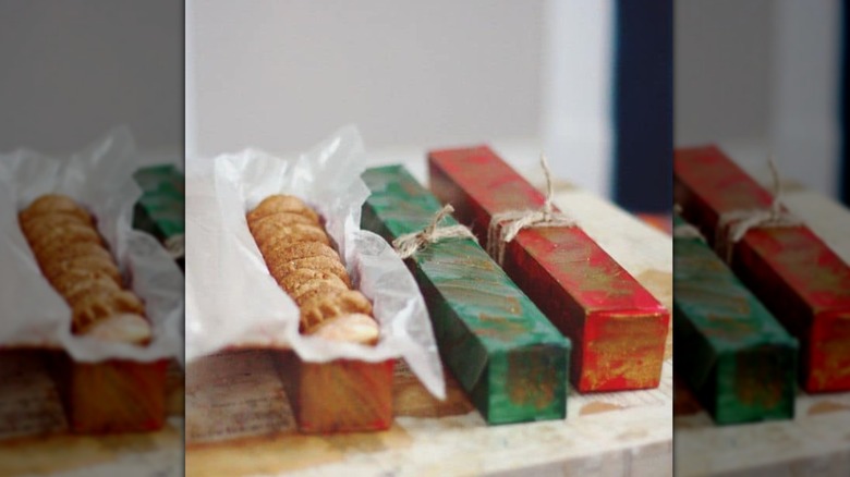 Three aluminum foil boxes in decorative wrappings with one open to show cookies arranged inside