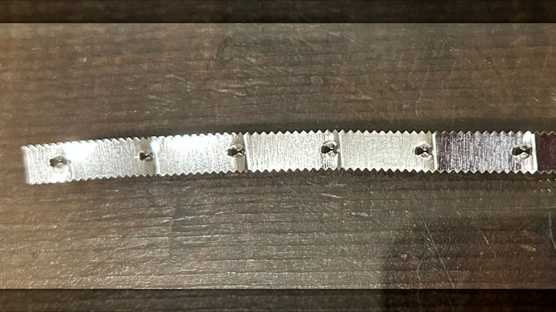 Metal blade removed from aluminum foil box sitting on dark wood surface