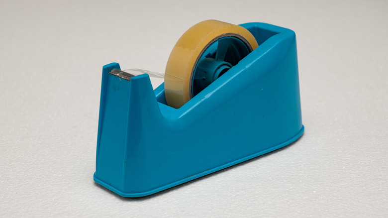 Blue tape dispenser with roll of clear tape inside on beige background