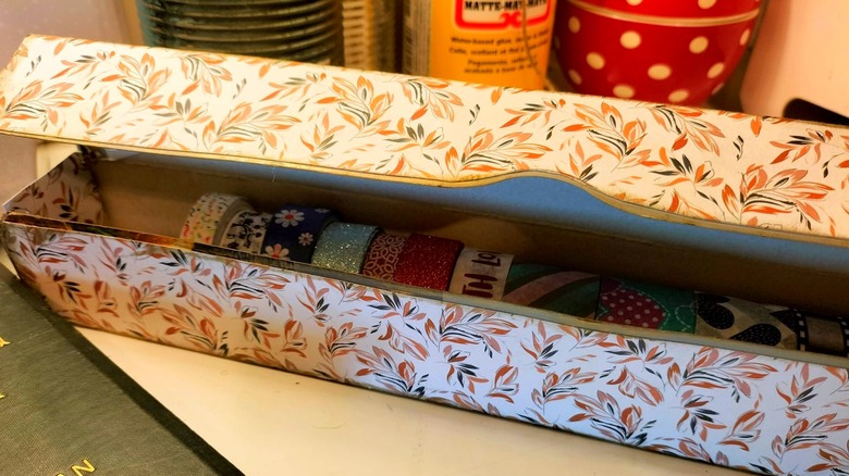 Aluminum foil box decorated with floral pattern with rolls of tape or ribbon arranged inside