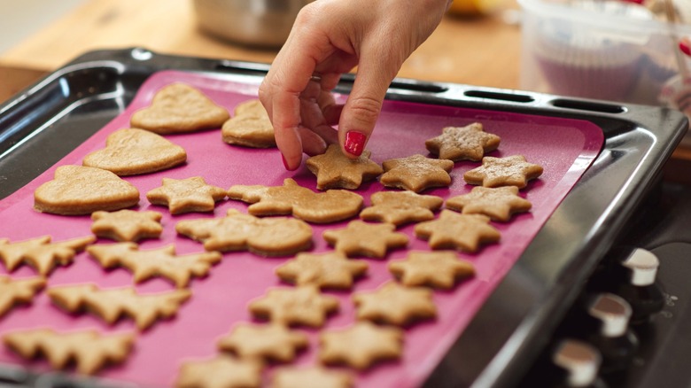 Hand taking baked cookies off of black sheet pan lined with pink silicone mat