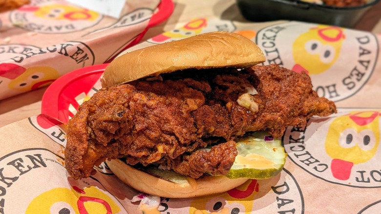 A hot chicken sandwich with slaw and pickles on Dave's Hot Chicken-branded paper