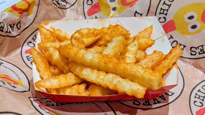Seasoned, crinkle-cut fries in a paper container on Dave's Hot Chicken-branded paper
