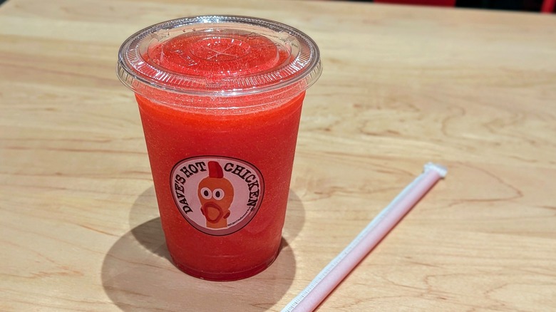 A red slushie in a plastic cup next to a straw on a light-colored wood table