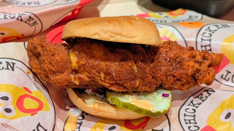 A hot chicken sandwich with slaw and pickles on Dave's Hot Chicken-branded paper