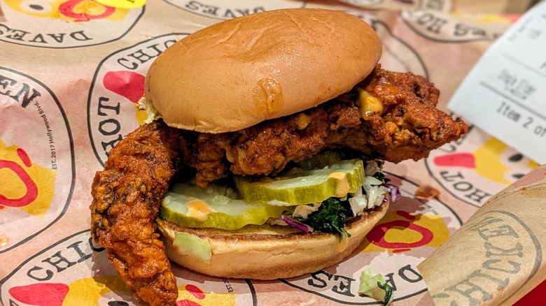 A hot chicken sandwich with slaw and pickles on Dave's Hot Chicken-branded paper