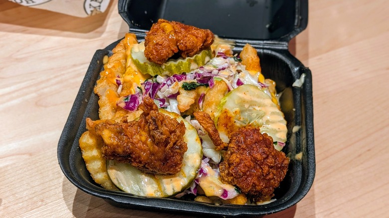 Chicken, pickles, and slaw on cheesy fries in a black take-out container