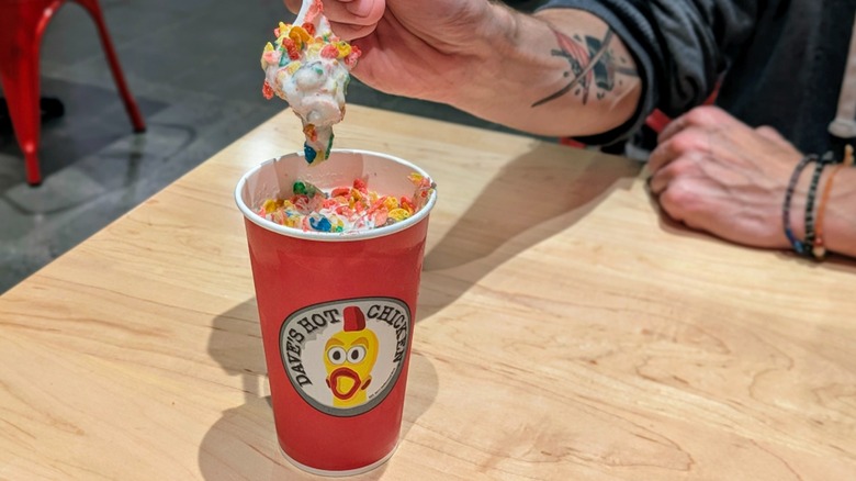 A hand scooping Fruity Pebbles and vanilla shake out of a paper cup at Dave's Hot Chicken