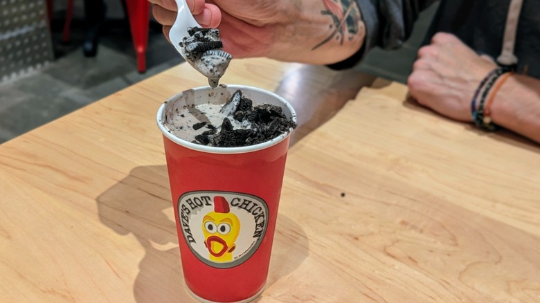 A hand scooping ice cream and Oreo pieces from a plastic cup at Dave's Hot Chicken