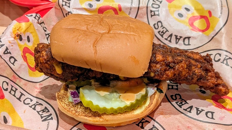 A hot chicken sandwich with slaw and pickles on Dave's Hot Chicken-branded paper