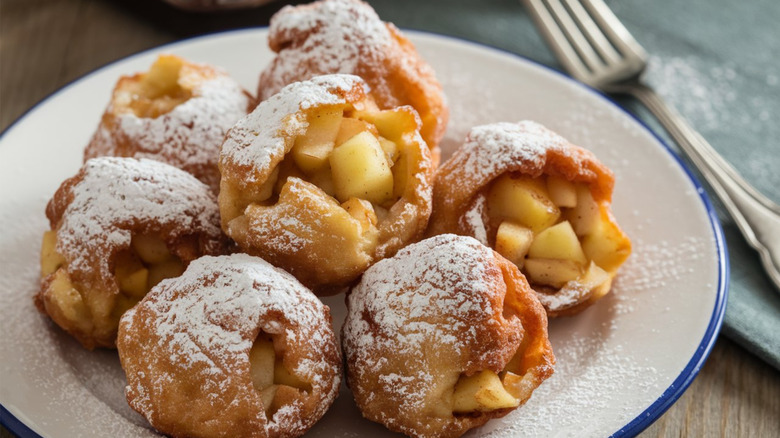 fried apple fritters with a coating of powdered sugar on a white plate