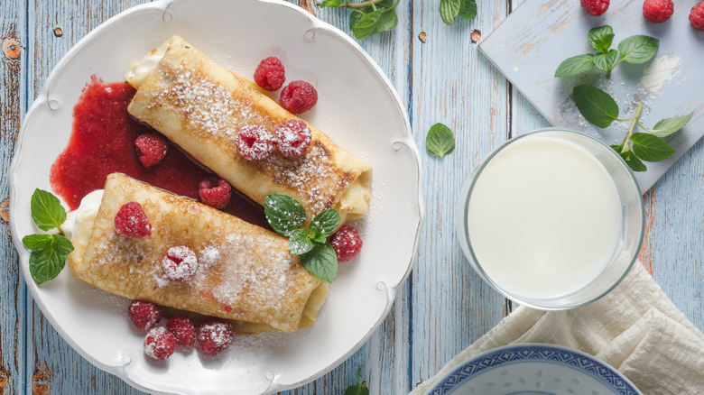 blintzes filled with sweet cheese with raspberries and compote on a white plate