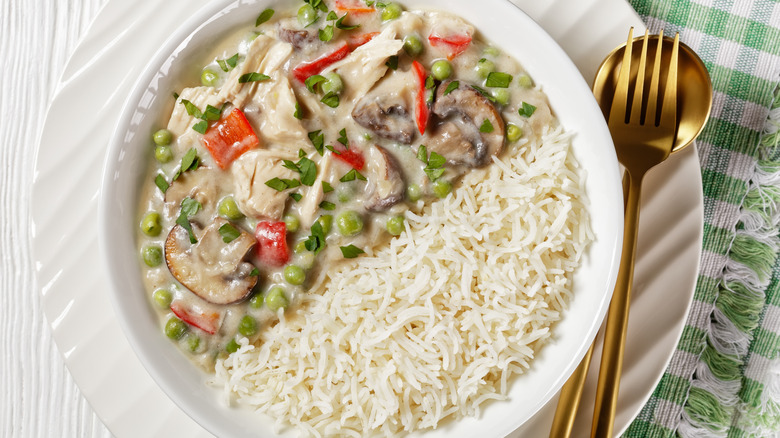 chicken a la king with rice in a white bowl next to gold cutlery