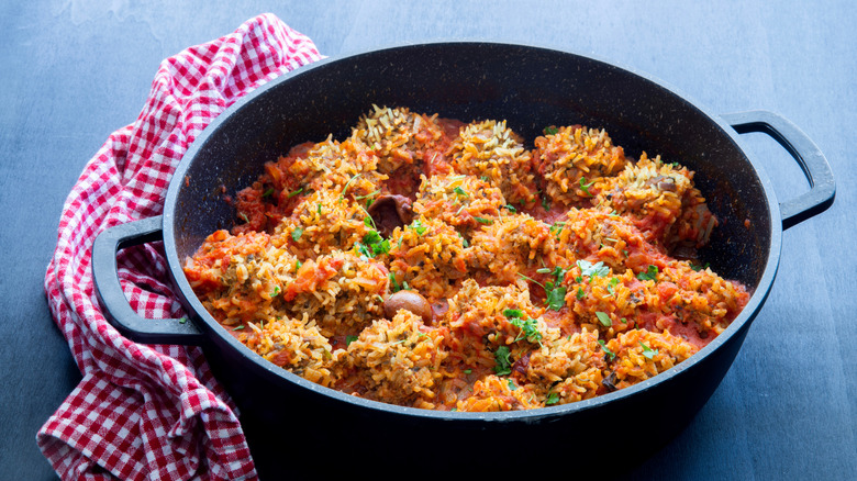 Porcupine meatballs in a black skillet next to red and white cloth on blue table