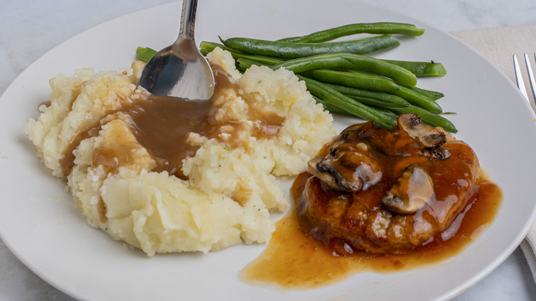 salisbury steak on a plate with mushrooms and onions seved with green beans and mashed potatoes
