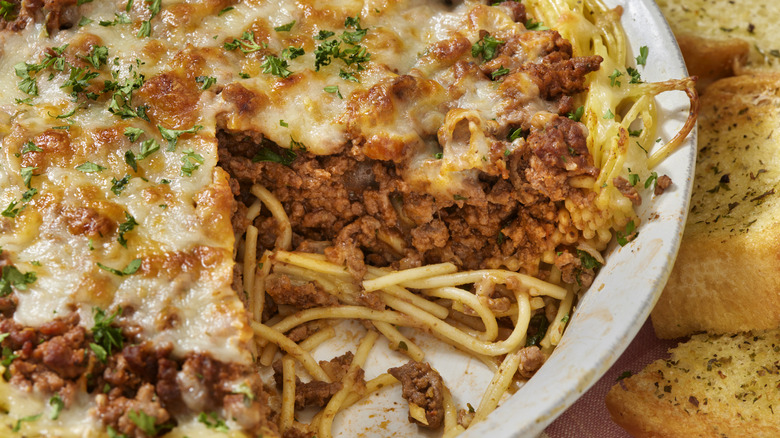 close up of spaghetti pie with slice removed next to garlic bread