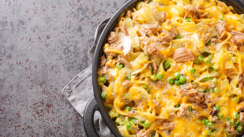 Tuna casserole with pasta, green peas, mushrooms and cheddar cheese close-up in a frying pan on the table