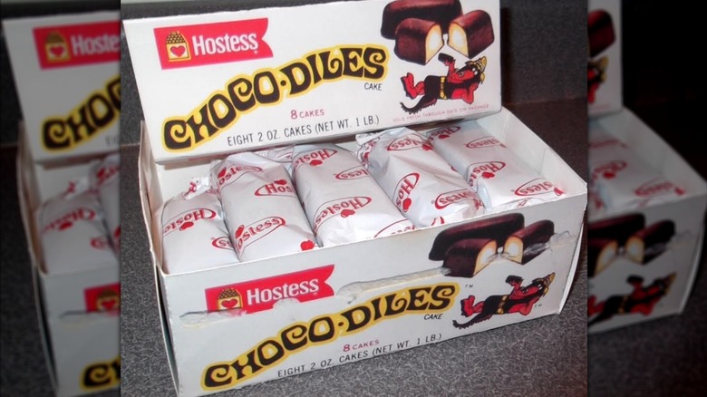 A white box filled with individually wrapped Hostess cakes with printed brand name "Chocodiles" along with a crocodile mascot and chocolate-covered yellow cake with cream filling