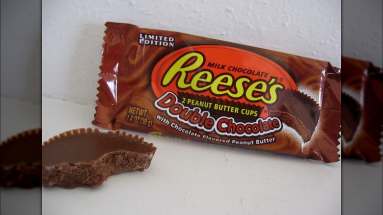 A packet of Reese's Double Chocolate peanut butter cups, next to a cup with a bite taken out of it.