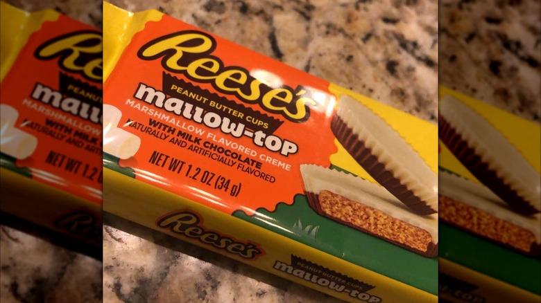 An orange and yellow packet of Reese's Mallow-Top peanut butter cups sitting on a granite countertop. The cups, pictured on the package, have a white top half and a brown chocolate bottom half.