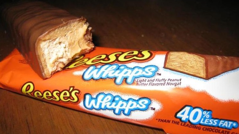 A cross-section of a Reese's Whipps candy bar, showing the peanut nougat inside. The bar sits on top of an orange and white wrapper showing the Reese's Whipps logo.