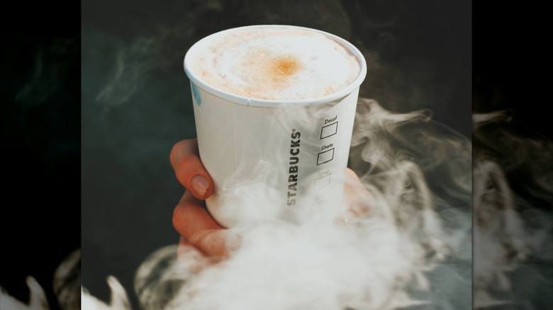 Hand holding a smoked butterscotch latte with smoke around it