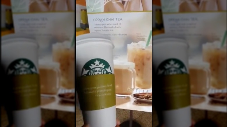 Hand holding Oprah Cinnamon Chai Tea Latte in front of advertisement for Oprah Chai Tea