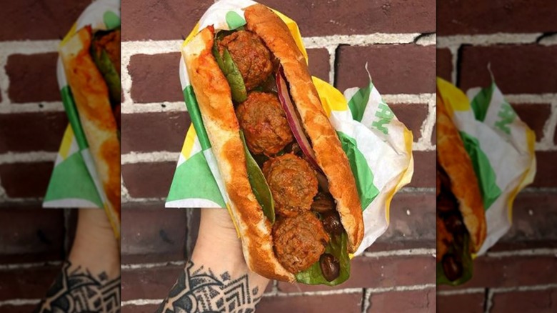 Tattooed arm holds up Beyond Meat Meatball Marinara sub against wall, mirrored image