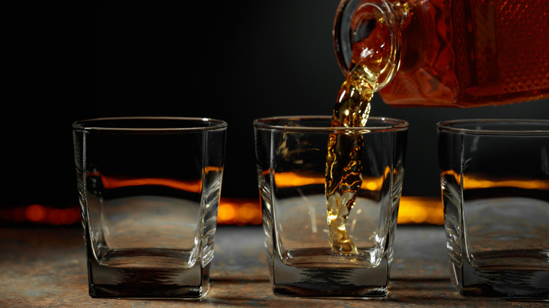 A bottle of brown liquor being poured into one of three glasses