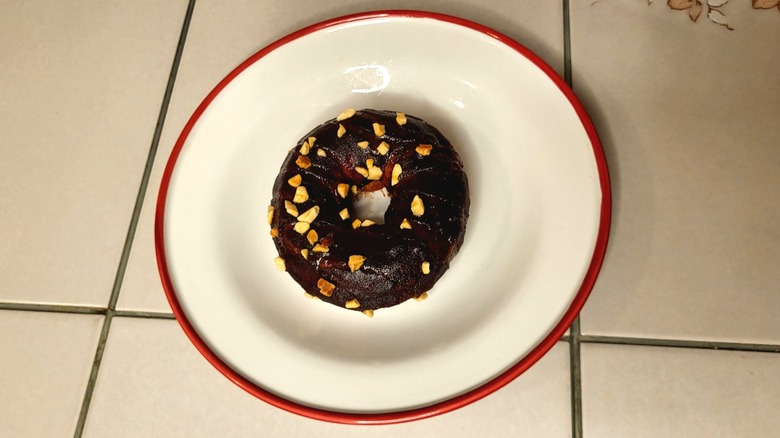 A donut topped with dark chocolate frosting and crushed peanuts.