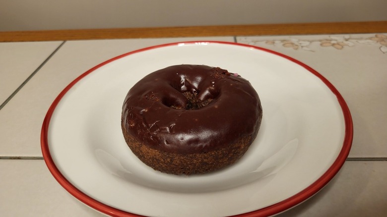 A chocolate cake donut with chocolate frosting on a white and red plate.