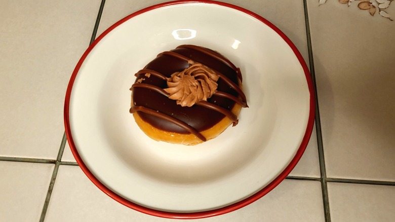 A donut topped with chocolate frosting, a chocolate drizzle, and a swirl of chocolate buttercream.