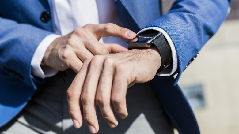 Close up of a man in a blue suit and white shirt looking at his black watch