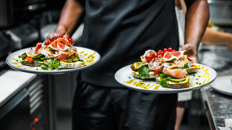 Close up of a person in black clothes carrying two dishes with salad