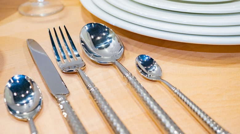 Close up shot of white plates and silver cutlery on a wooden table