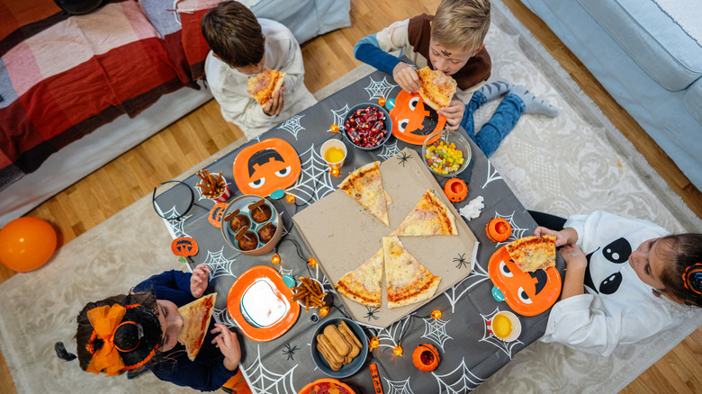 Kids sitting around a table eating pizza while celebrating Halloween