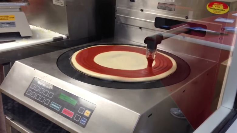 Costco pizza robot applying sauce to dough