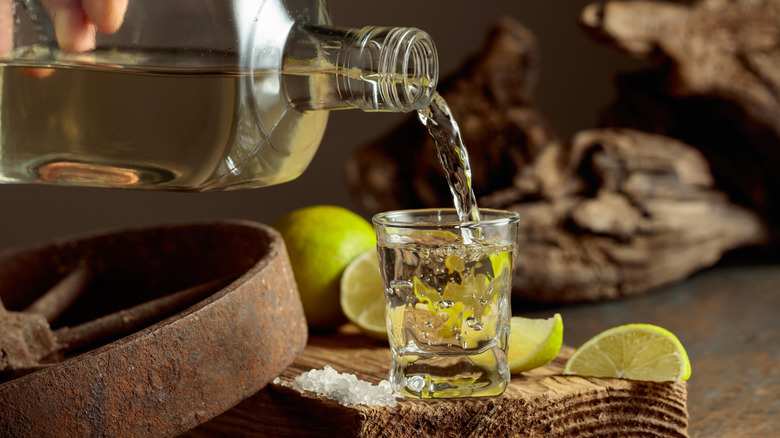 Hand pouring tequila into shot glass with limes