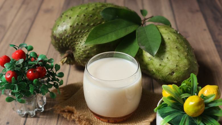 Glass of soursop juice with fresh soursop and colorful fruits in small vases