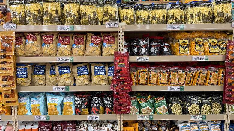 Rows of variously flavored potato chips, corn puffs, and similar savory snacks on the shelves at a Trader Joe's store.