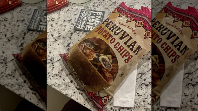 A bag of Peruvian potato chips on a granite countertop along with a drink in a cocktail glass. A window into the bag shows red and purple-tinted chips.