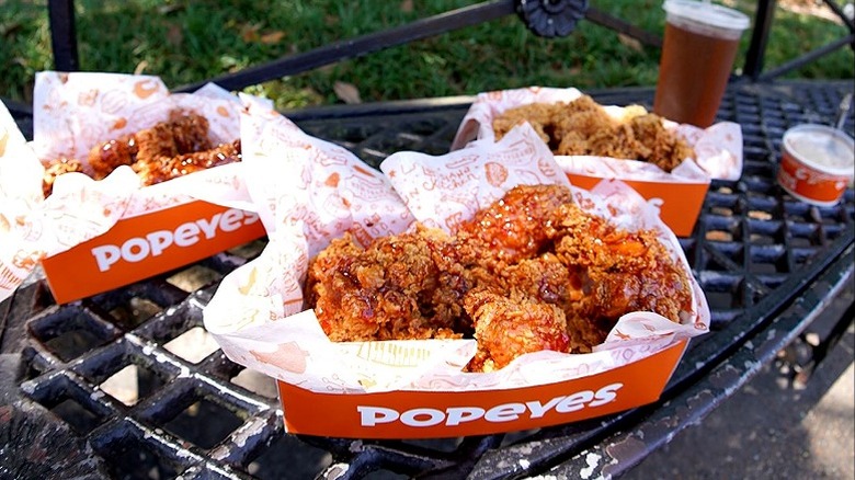 A few containers of Popeyes fried chicken arranged on bench.