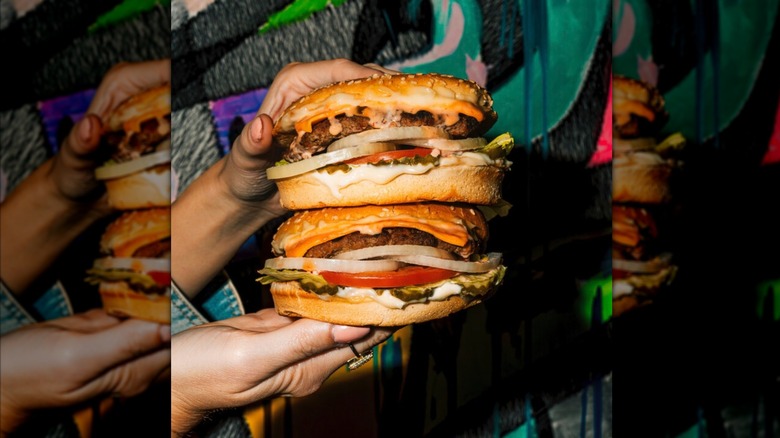 A person holding two Carl's Jr burgers stacked on top of each other
