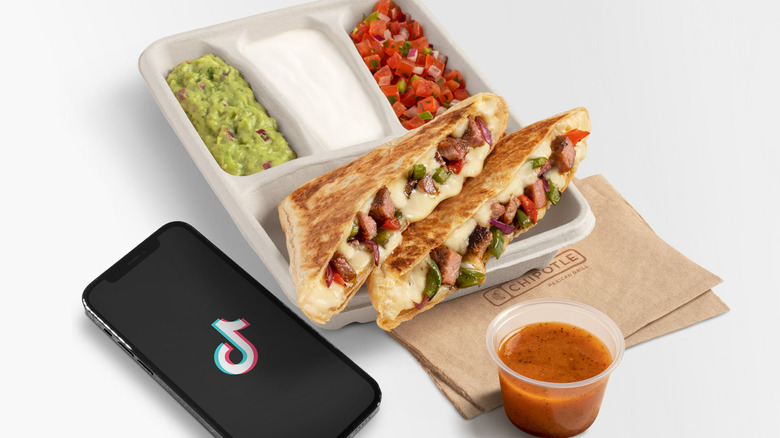 The Keithadilla Chipotle Fajita Quesadilla with a phone with the TikTok logo and Vinaigrette on the side against white background