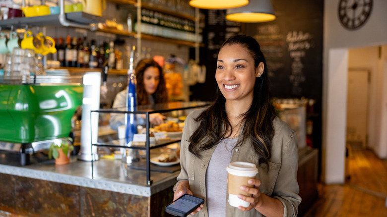A woman leaves a cafe with a to-go cup of coffee in her hand