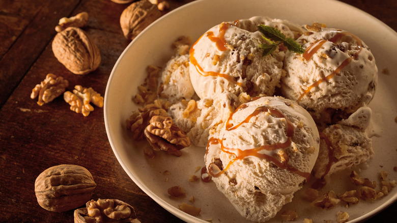 Scoops of maple walnut ice cream drizzled with caramel sauce and garnished with walnuts in large bowl