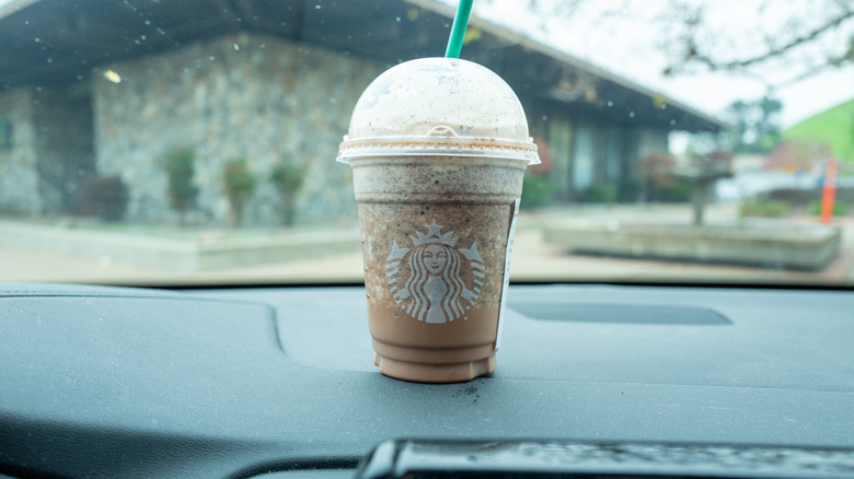 a Starbucks Frappuccino, siting on the dash of a car in California, with a mid-century modern home dimly visible through the windshield