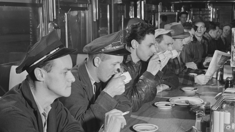 men drinking coffee at a blue-collar diner in the 1950s, in a vintage black-and-white photo